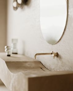 a bathroom sink sitting under a round mirror next to a wall mounted faucet