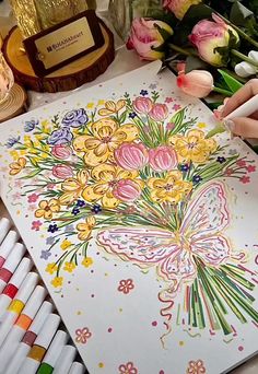 a person is drawing flowers on paper with crayons and colored pencils next to them