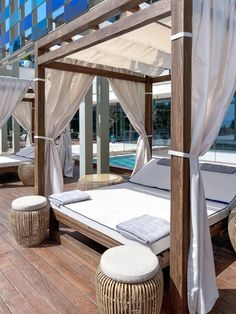 a bed sitting on top of a wooden floor next to a swimming pool with white drapes