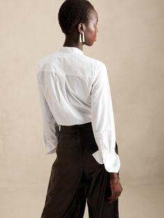 A seamless silhouette, this soft tuxedo shirt is made from 100% cotton with a concealed button front, elegant pintuck detail and exaggerated cuffs.  SEMI-FITTED: Cut for a not-too-tight, not-too-loose fit.  Banded collar.  Hidden button front.  Troca Timeless Daywear Tops With Placket, Timeless Long Sleeve Tops With Concealed Placket, Timeless Relaxed Fit Tops With Button Cuffs, Timeless Relaxed Fit Top With Button Cuffs, Timeless Tops With Placket For Daywear, Relaxed Fit Top With Button Cuffs, Chic White Tops With Concealed Placket, Elegant Shirt With Placket And Shirttail Hem, Timeless Button-up Top With Hidden Buttons