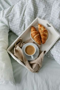 two croissants and a cup of coffee on a bed