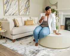 a woman sitting on top of a round table in front of a couch and fireplace