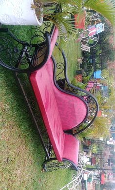 a pink bench sitting on top of a green grass covered park area next to a potted plant