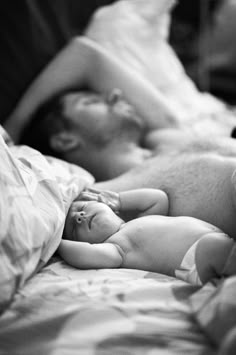 a black and white photo of a baby sleeping on someone's back in bed