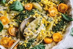 a bowl filled with pasta and vegetables on top of a white tablecloth next to a silver spoon