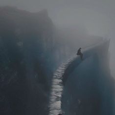 a person standing on the edge of a cliff in the middle of foggy weather