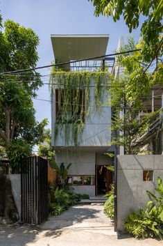 the house is surrounded by greenery and concrete walls, with an iron gate leading to it