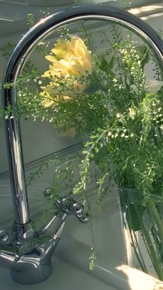 yellow flowers in a clear glass vase on a sink faucet with water running from it