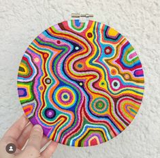 a person holding up a colorful circular artwork piece