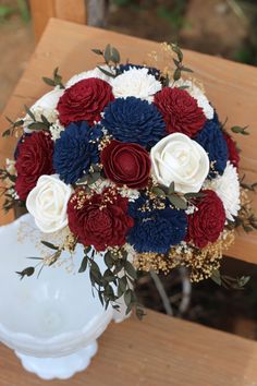 a bridal bouquet with red, white and blue flowers on a wooden bench outside