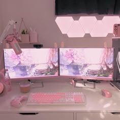 two computer monitors sitting next to each other on top of a white desk with pink keyboard and mouse