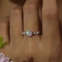 a woman's hand with a ring on it and a flower in the background