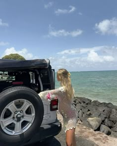 a woman standing next to a parked jeep near the ocean