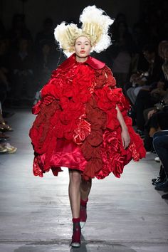 a woman in a red dress with flowers on her head walking down the catwalk