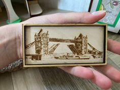 a person holding up a small wooden box with a drawing of the tower bridge on it