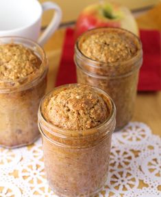 three glass jars filled with food sitting on top of a doily next to an apple