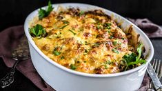 a casserole dish with cheese and parsley on the side next to a fork