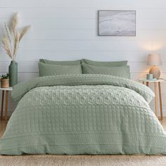 a bed with green bedspread and pillows in a white room next to a lamp