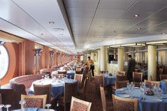 a dining room with blue tablecloths and white plates on the tables in front of a large window