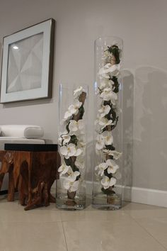 two glass vases with flowers in them on the floor next to a wooden table