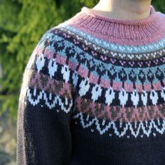 a woman wearing a pink and black sweater standing in front of some green bushes with her eyes closed