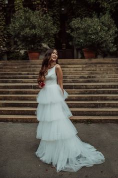 a woman standing in front of some steps wearing a white wedding dress with tiered layers