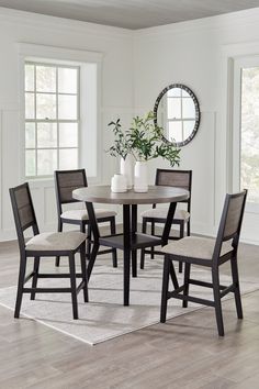 a dining table with four chairs and a vase on the table in front of it