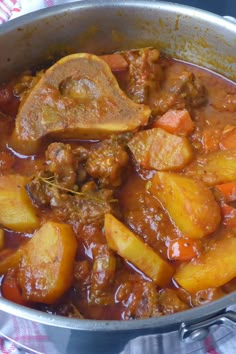 a pot filled with meat and vegetables on top of a tablecloth next to a wooden spoon