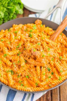 a skillet filled with pasta and meat sauce on top of a striped towel next to parsley