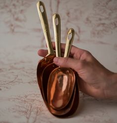 a hand holding three gold spoons in a brown holder on a white tablecloth