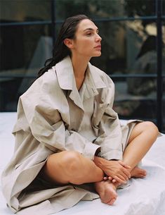 a woman sitting on top of a bed next to a window in a gray dress