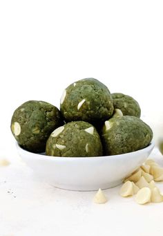 a white bowl filled with green cookies on top of a table next to some cashews