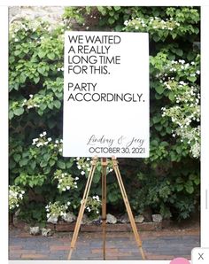 a white sign sitting on top of a wooden easel next to a lush green wall