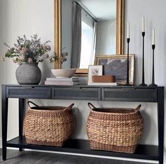 two wicker baskets under a console table with a mirror and candles in the background