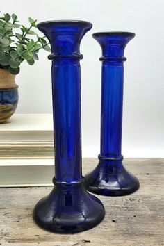 two blue glass vases sitting on top of a wooden table next to a potted plant