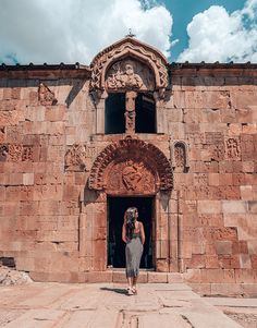 a woman standing in front of a stone building with an arch above her head and doorway