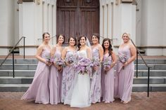 a group of women standing next to each other in front of a building holding bouquets