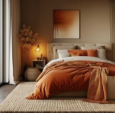 a bed with an orange comforter and pillows in a room next to a window