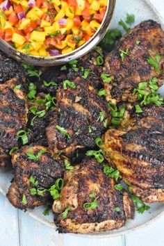 grilled meats and vegetables on a plate with a bowl of salad in the background