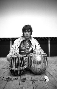 a man sitting on the ground with two large drums in front of his face and hands