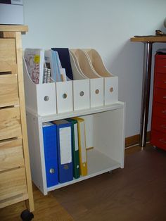 a white shelf with file folders and binders on it next to a red dresser