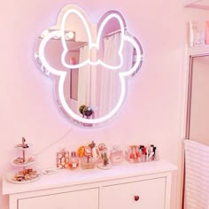 a white dresser topped with a mirror next to a wall mounted shelf filled with cosmetics