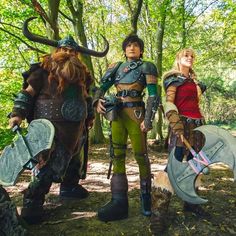 three people dressed up in costume standing next to each other on the forest floor with trees and foliage behind them