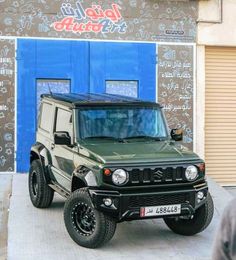 a green jeep is parked in front of a building with graffiti on it's walls