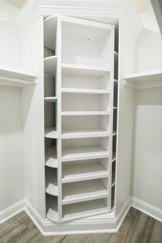 an empty closet with white shelves and wood flooring