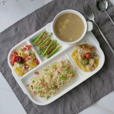 a white plate topped with lots of food next to a bowl of soup and a fork