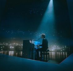 a man sitting at a piano in front of a microphone on stage with lights behind him