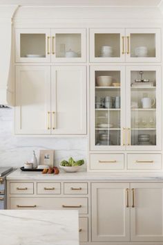 a kitchen with white cabinets and marble counter tops, gold trim on the glass doors