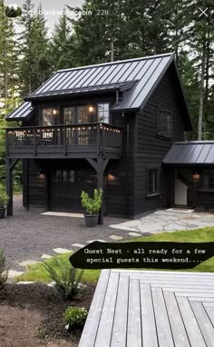 a black house with lots of windows and lights on the front porch is surrounded by pine trees