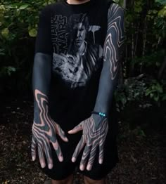 a man with tattoos on his arms and hands is standing in front of some trees